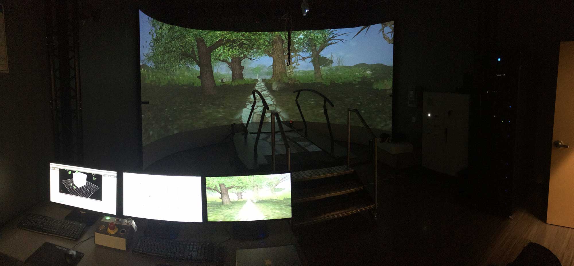 A virtual reality cobblestone trail in a forest displays on the enormous curved screen that surrounds the rehab treadmill