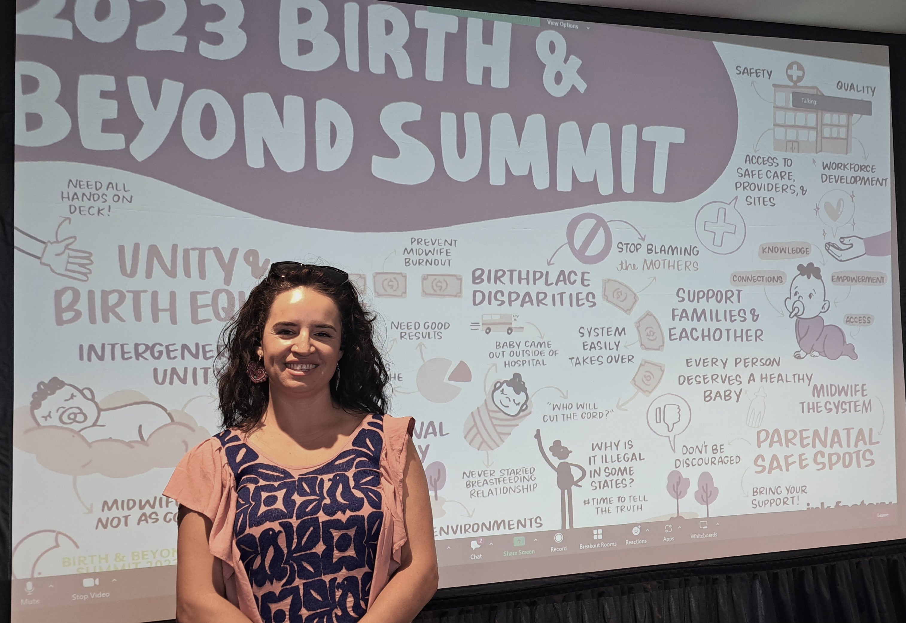 Frida stands in front of large screen projecting the infograph created during the 2023 Birth and Beyond Summit