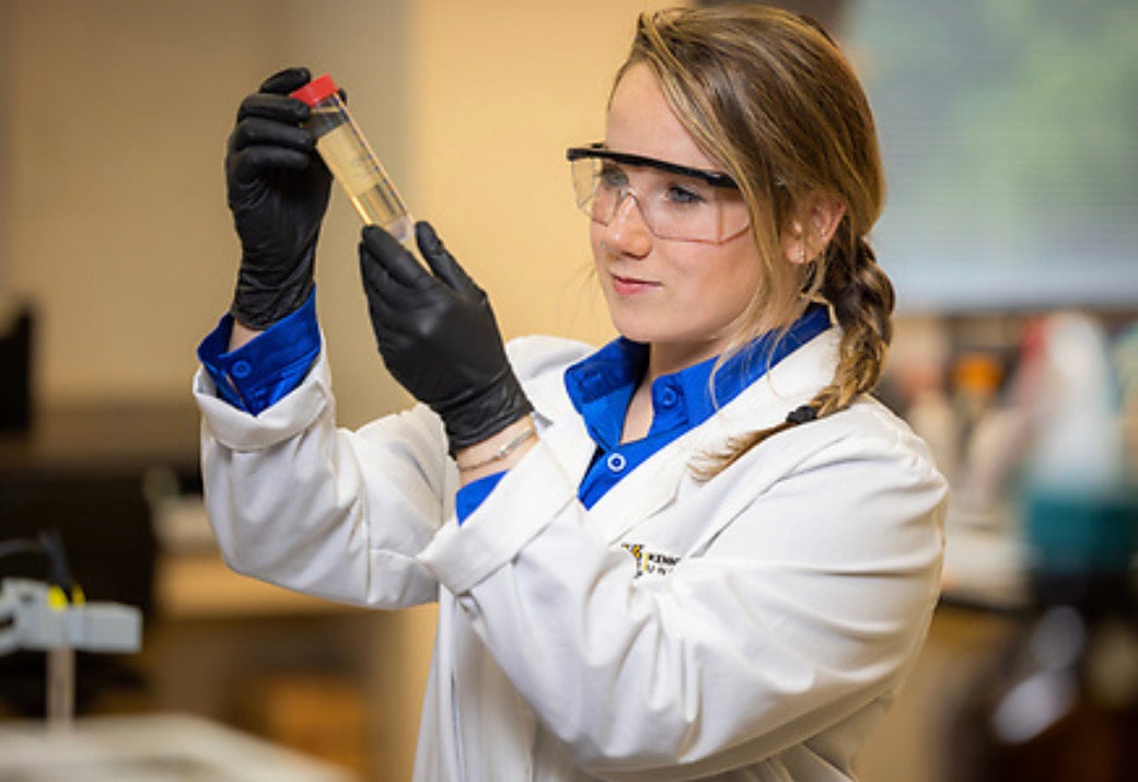 A researcher looking at samples in a lab coat with goggles and gloves on.