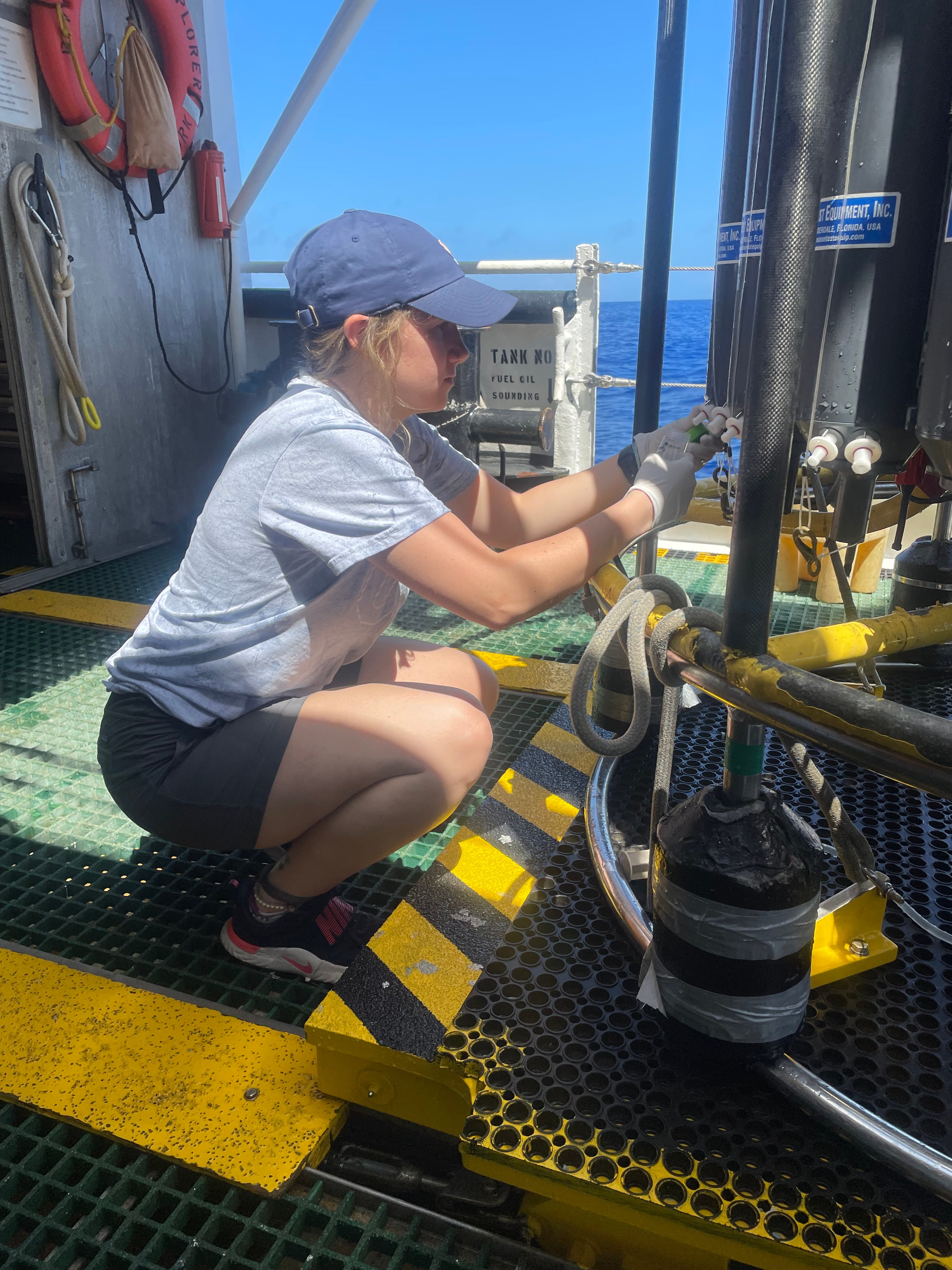 A researcher is crouched down sampling ocean water from large tubes.