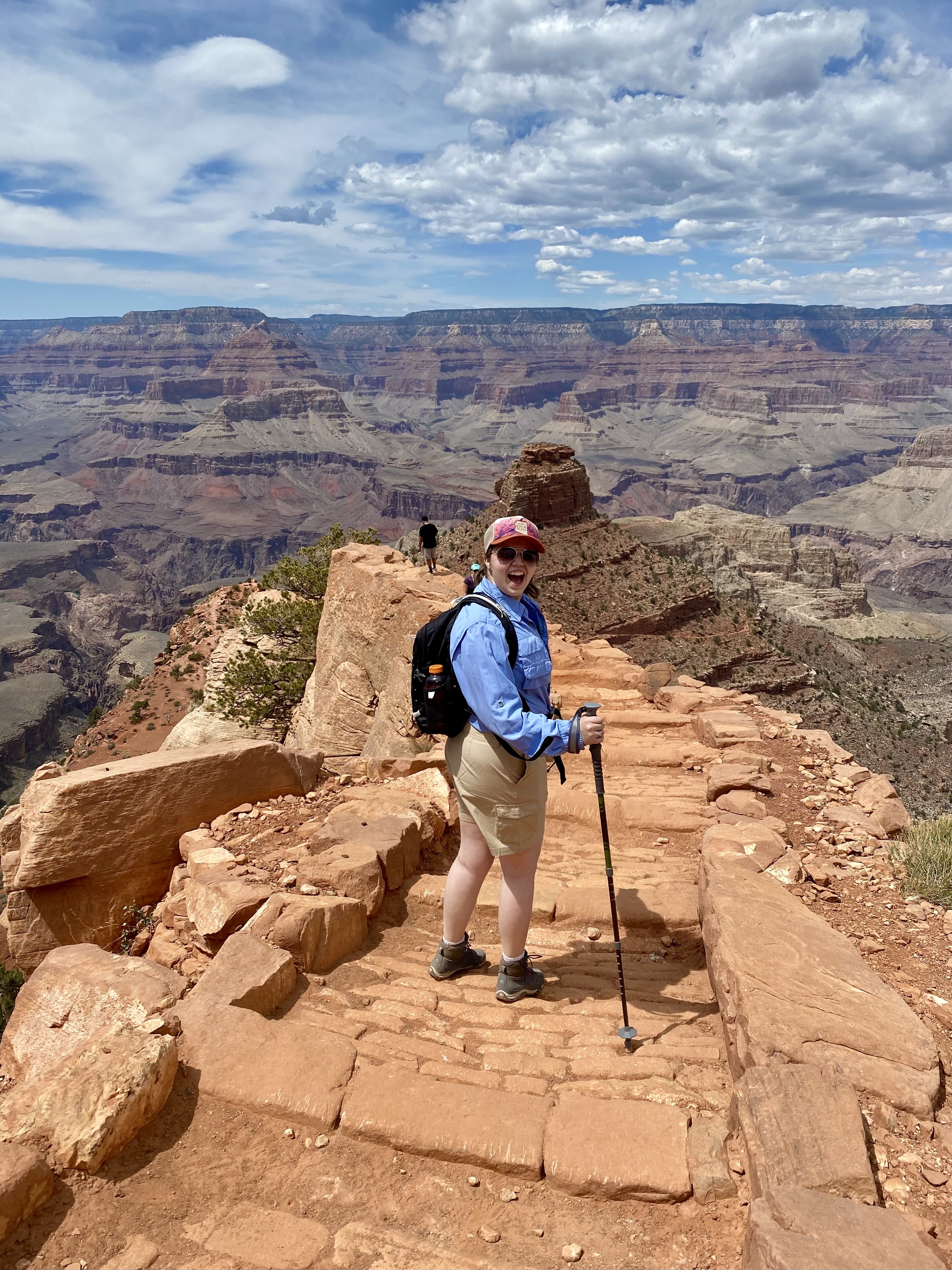 Emily hiking into Grand Canyon, looking back at the camera with the canyon in full view behind her. 