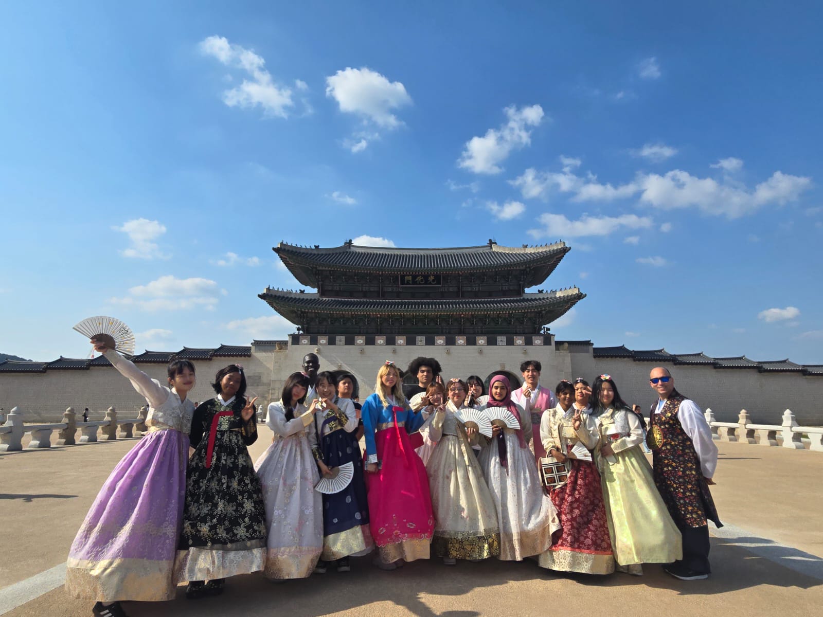 A group of students, dressed in traditional Hanboks, standing in front of the Gyeongbokgong Palace in Seoul, Korea