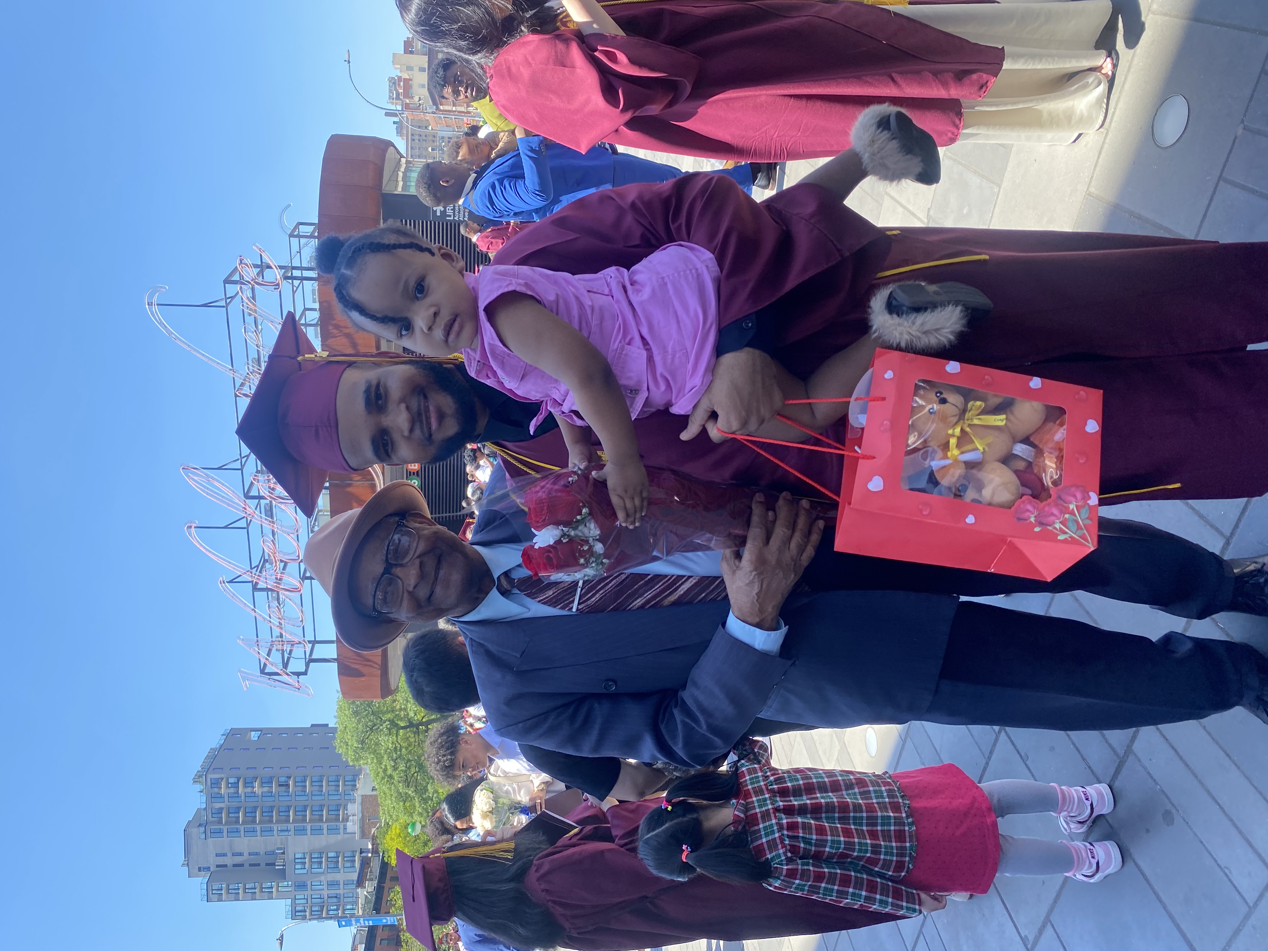 Cassagnol poses happily in his graduation gown and cap while holding his Daughter and standing besde his father