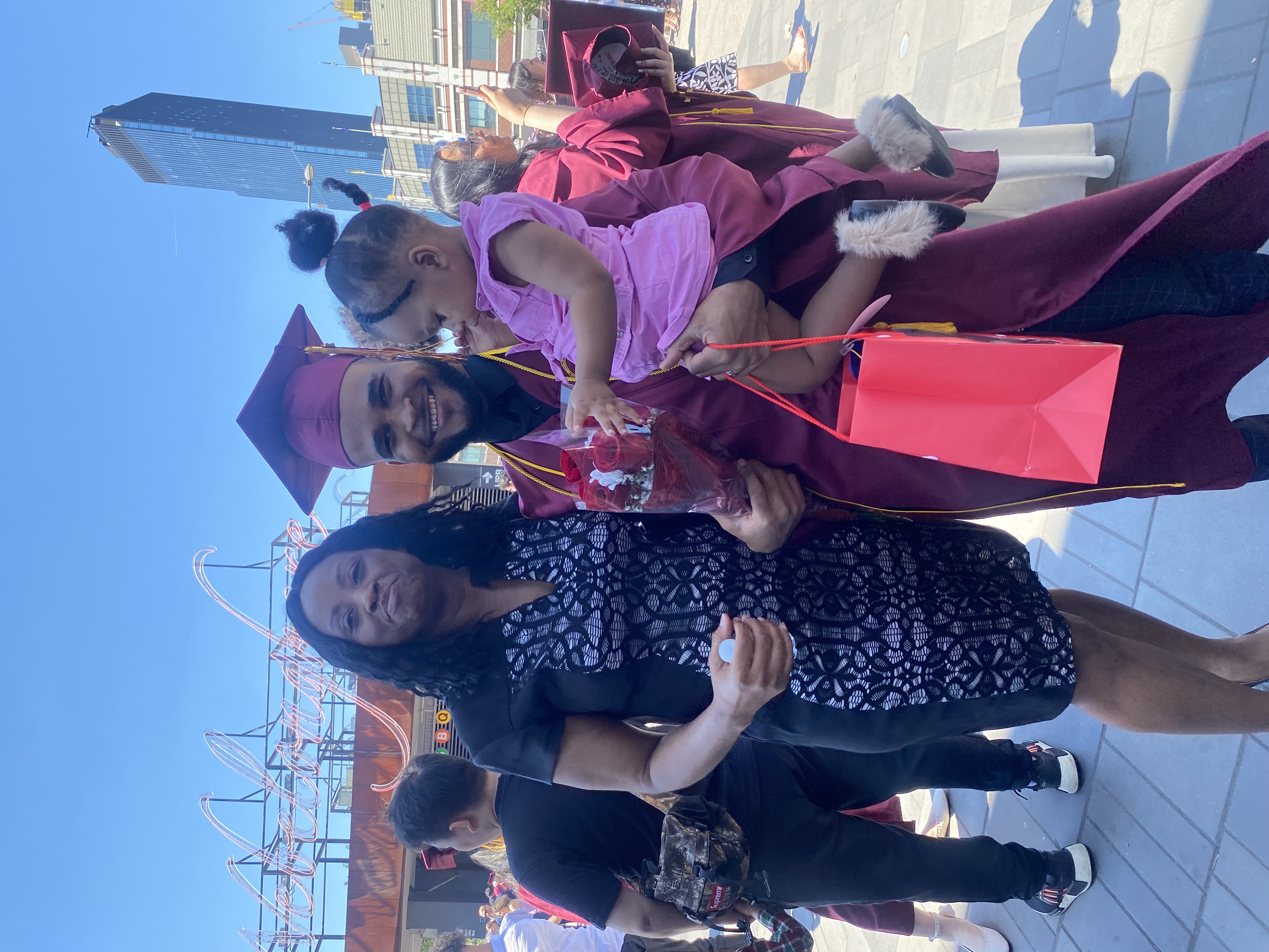 Clauny Cassagnol poses happily in his graduation gown and cap, holding his Dauighter and standing beside his older sister 